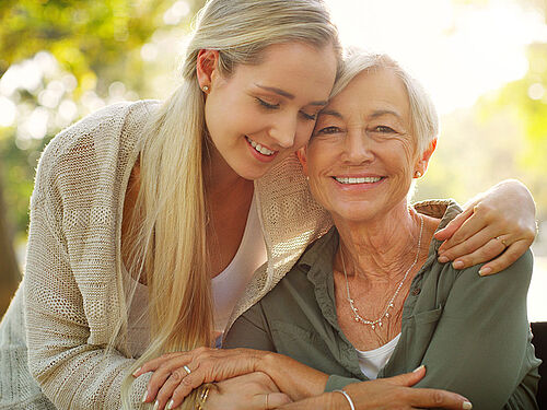 Ung kvinde som krammer sin mor i smuk natur, de smiler begge