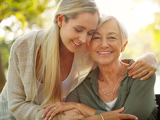 Ung kvinde som krammer sin mor i smuk natur, de smiler begge