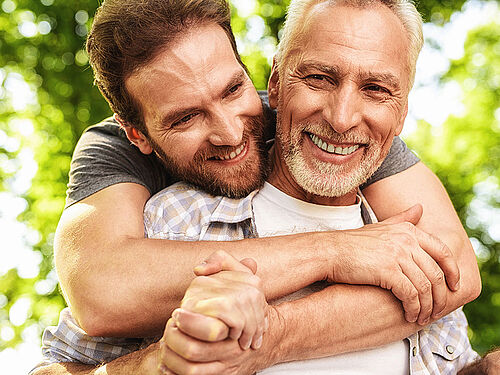 Дорослий чоловік обіймає свого літнього батька та посміхається